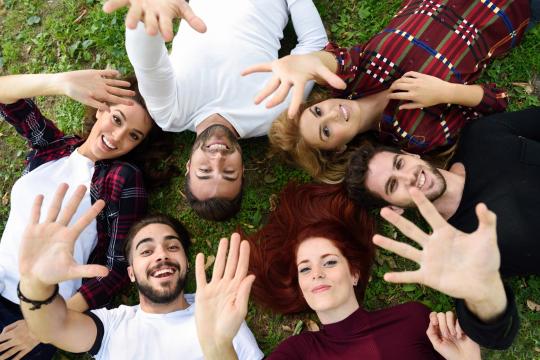 Plusieurs étudiants couchés sur l'herbe tendent leur main vers le ciel 